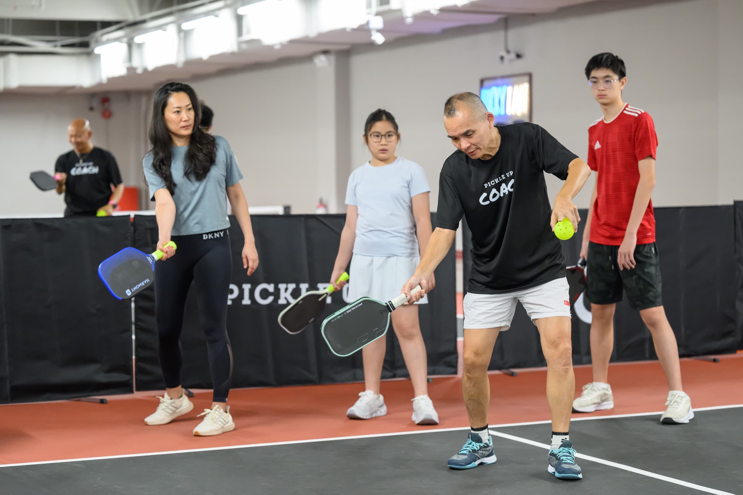 Head Coach SQ demonstrating a forehand to a group class, players following with paddles out.