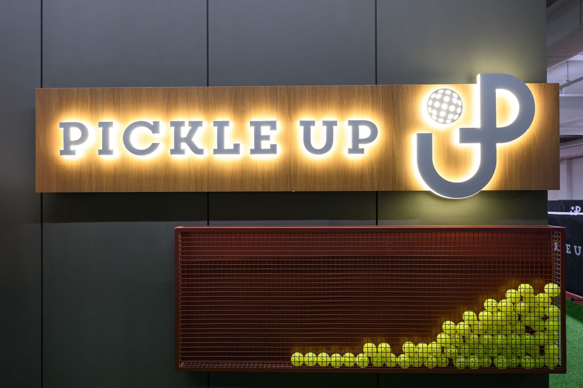 The lit Pickle Up sign on the wood panel at our entrance, above a terracotta cage full of balls.