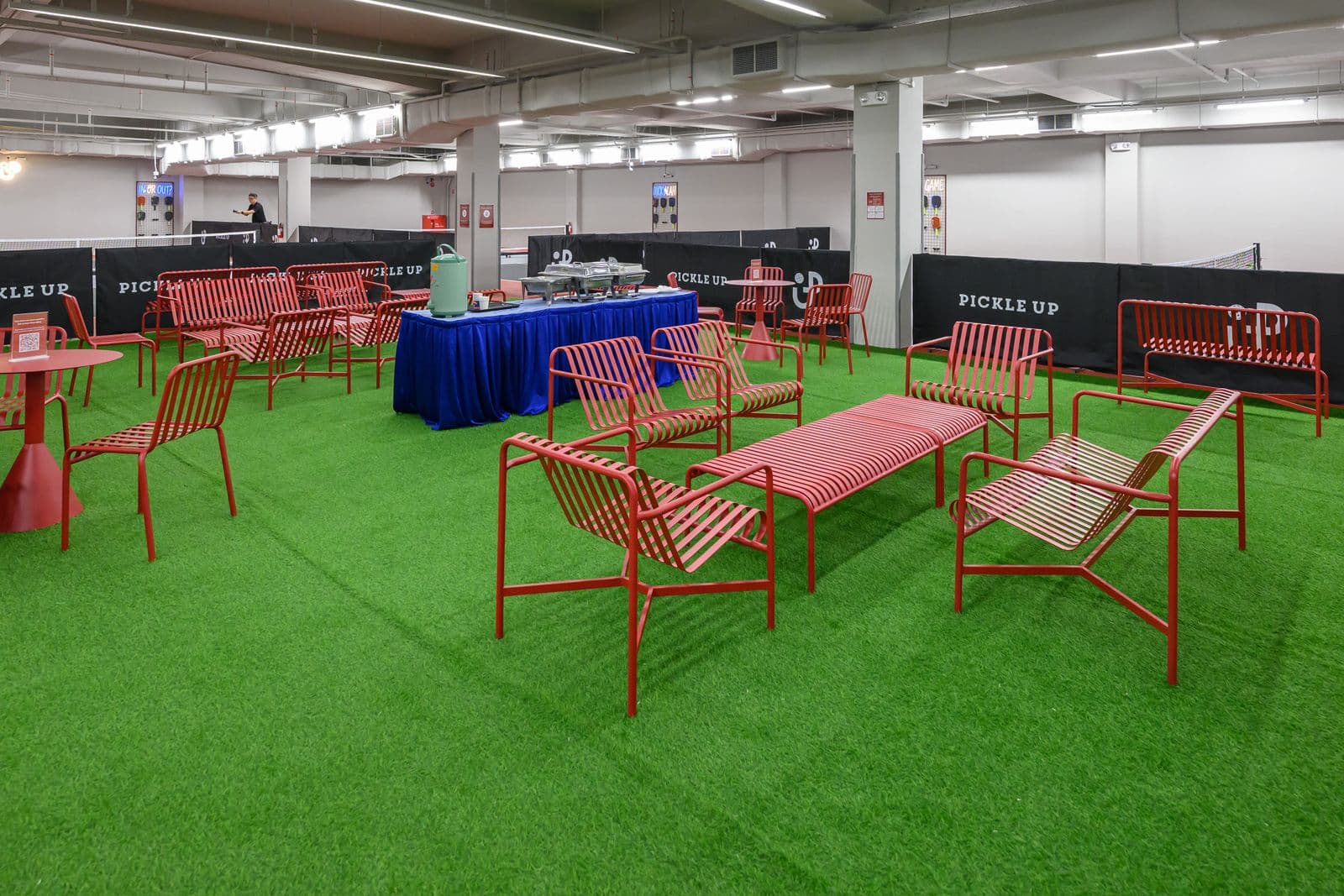 The lounge: red benches and tables on green turf beside the courts.