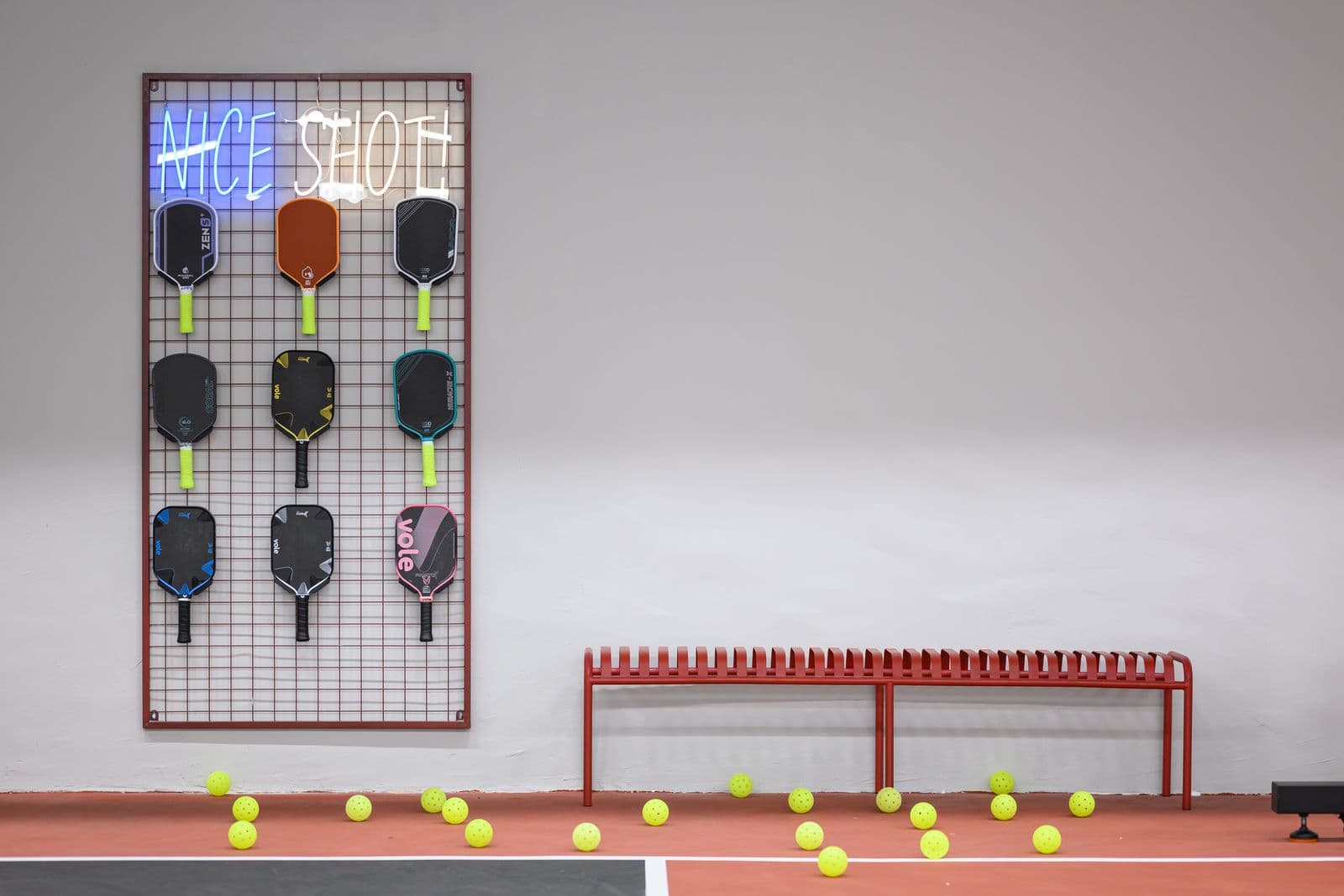 The paddle wall: demo paddles under a Nice Shot neon sign, a bench and loose balls below.